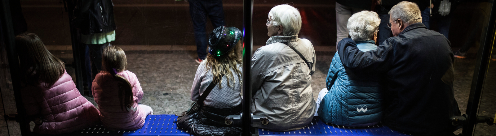 Junge und alte Menschen sitzen im Jahr 2018 auf der Bank einer Bushaltestelle in Berlin
