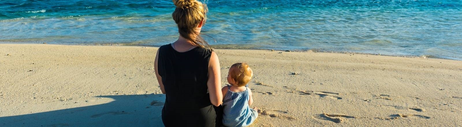 Eine Frau und ein Kind sitzen am Strand und schauen auf das Meer