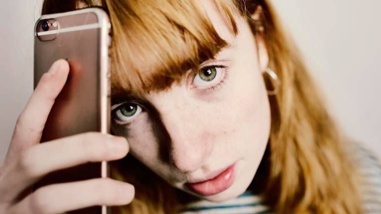 Frau mit roten Haaren hält Smartphone an ihren Kopf.