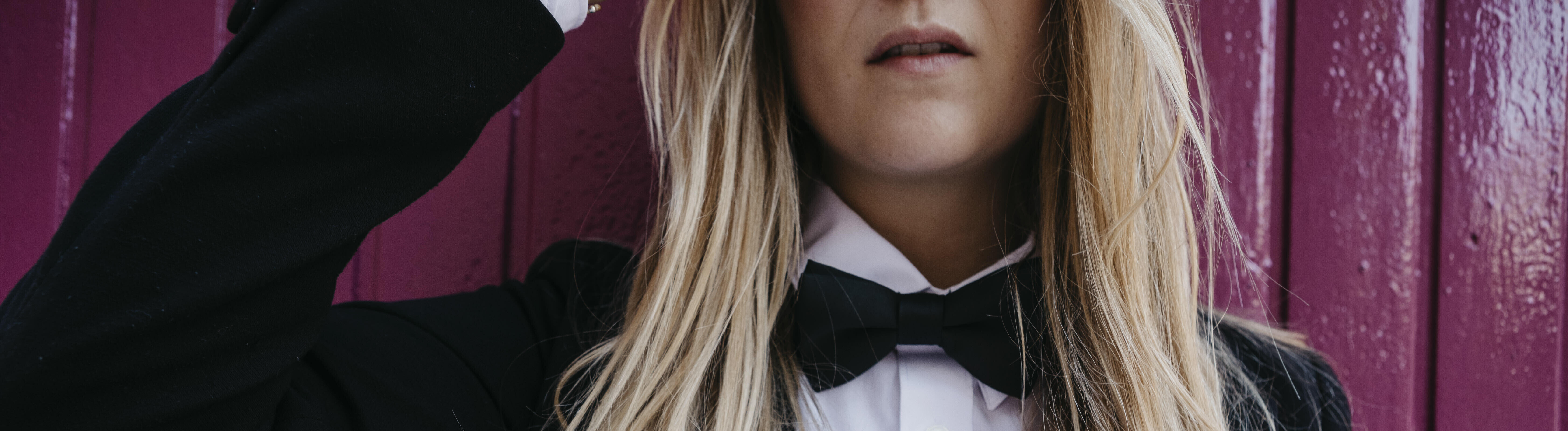 Eine Frau mit langen blonden Haaren in schwarzem Anzug mit Fliege