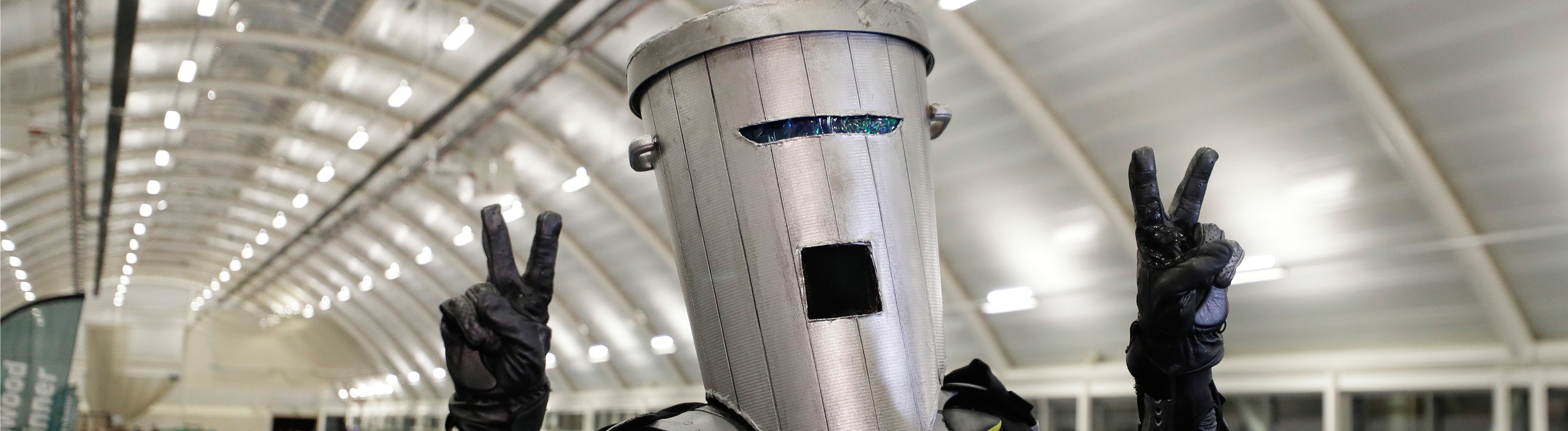 Ein Mann in Superheldenkostüm und einer Mülltonne auf dem Kopf hebt beide Hände als "Victory"-Zeichen in die Höhe.