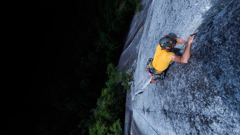 Ein Mann klettert eine steile Felswand hoch.