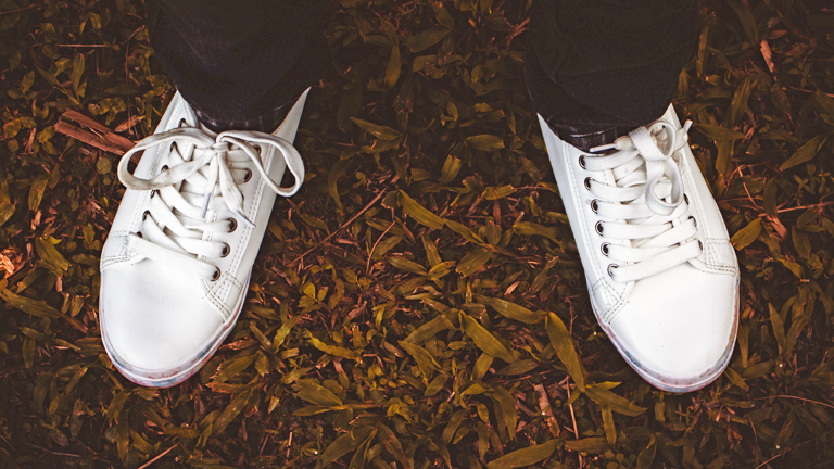 Zwei weiße Sneaker-Schuhe auf Laub und kleinen Ästen.