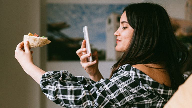 Eine Frau macht ein Handyfoto von ihrem Brötchen.