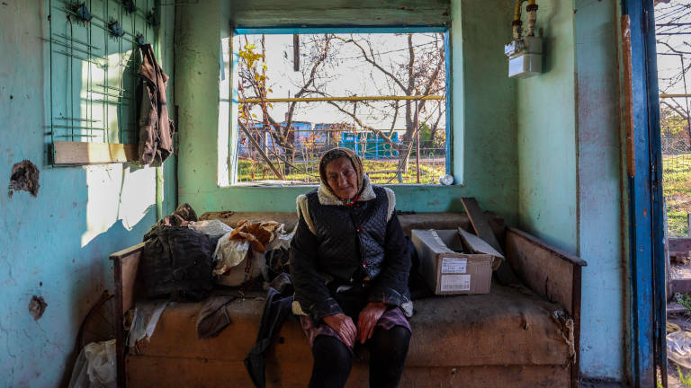 Eine alte Frau sitzt in ihrem zerstörten Haus auf einem Sofa