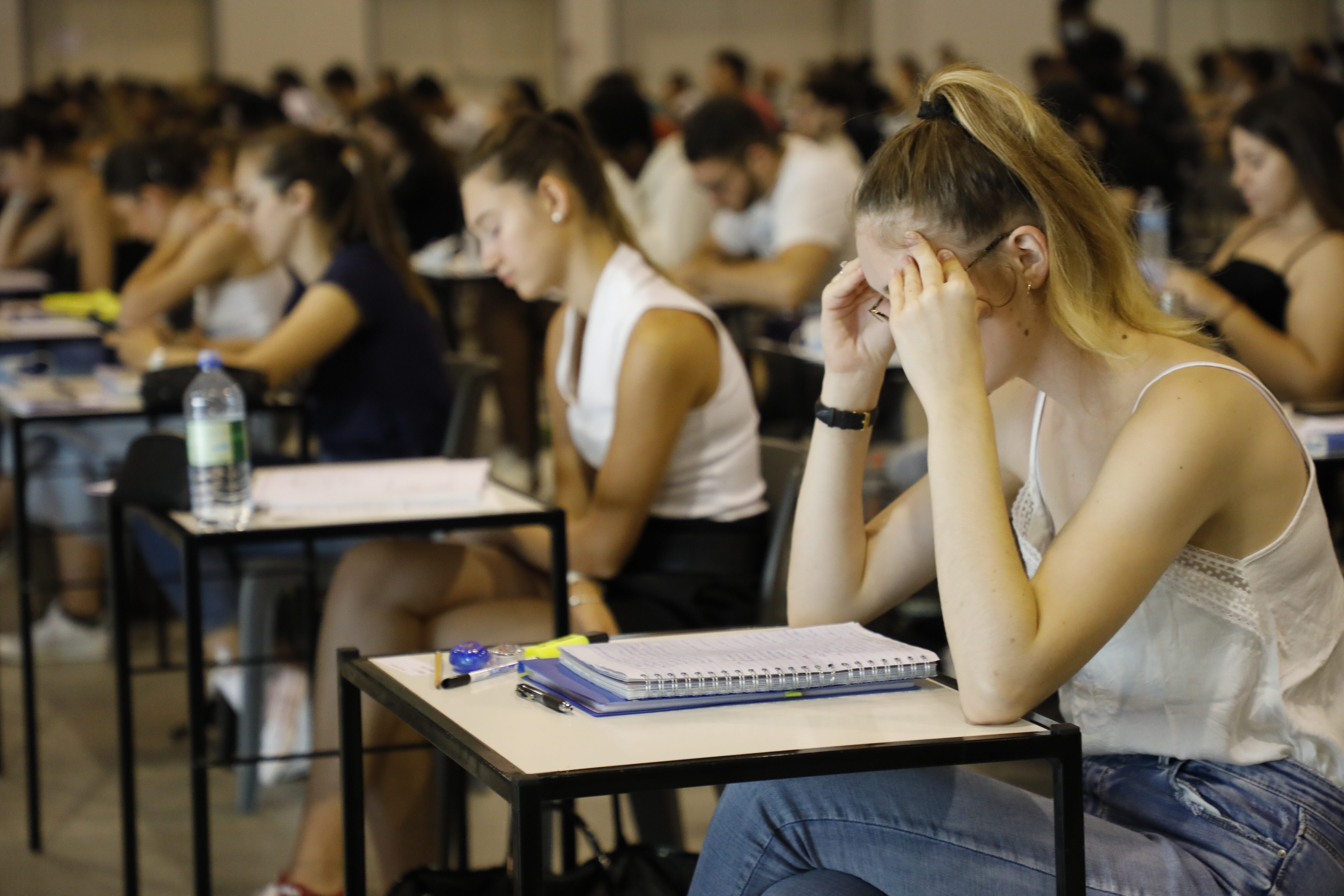 Ein Hörsaal mit Studierenden bei einer Prüfung, eine junge Frau vorne stützt ihren Kopf in den Händen ab