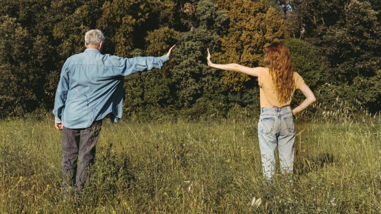 Mann und Frau stehen auf einer Wiese und zeigen eine Armlänge Abstand zueinander