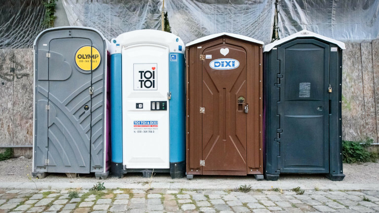 Im Bild sind verschiedene mobile Toiletten an einer Straße zu sehen.
