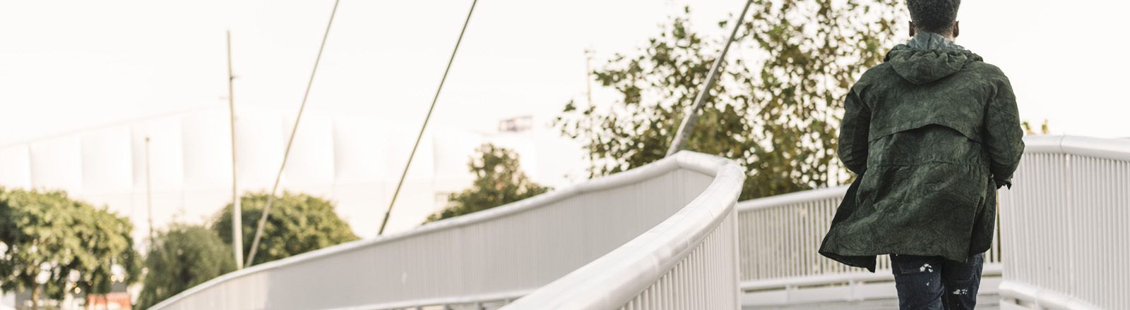 Ein Schwarzer Mann läuft über eine Brücke in einer Stadt, er ist nur von hinten zu sehen