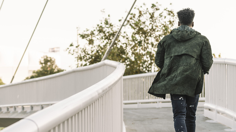 Ein Schwarzer Mann läuft über eine Brücke in einer Stadt, er ist nur von hinten zu sehen