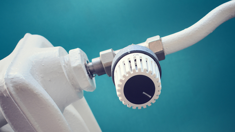 Eine weiße Heizung mit Thermostat vor einer grün-blauen Wand.