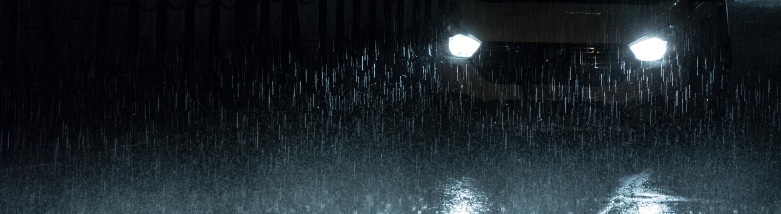 Scheinwerfer eines Autos bei Nacht und im Regen.
