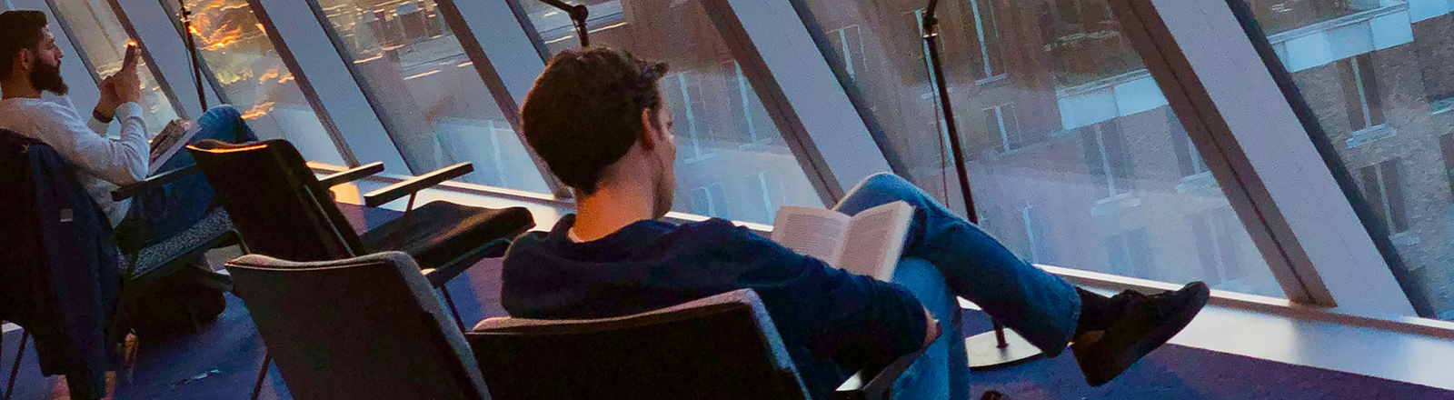 Bibliothek der Uni Groningen: Zwei Männer sitzen auf Sesseln und lesen. Vor ihnen ist ein Fensterpanorama mit Blick auf eine Stadt.