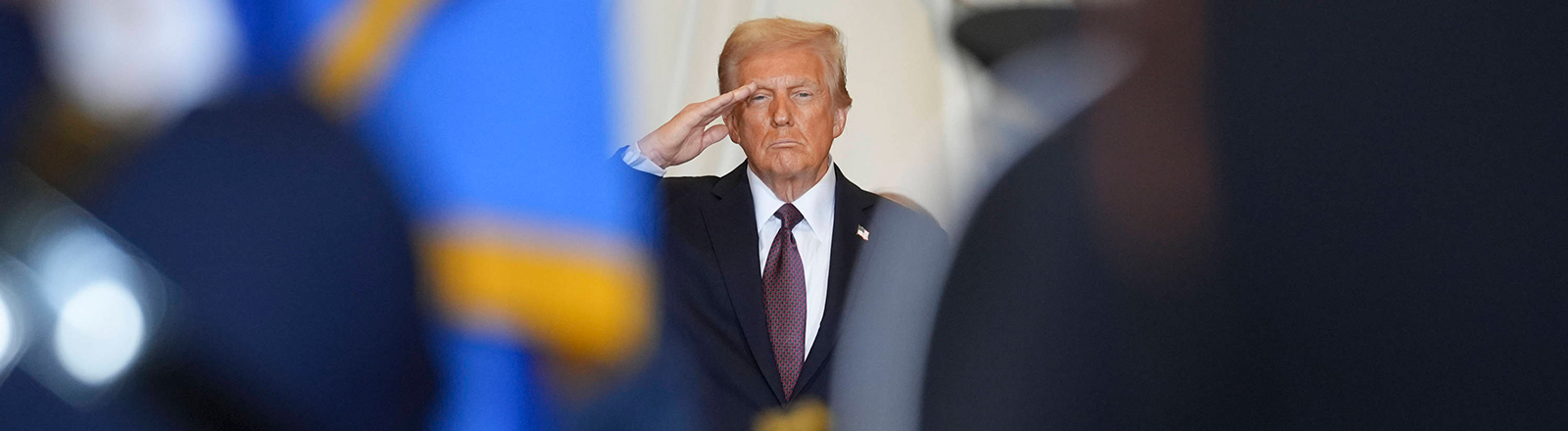 Links und rechts stehen Personen in Uniform. Zwischen ihnen ist eine Lücke. Der Blick fällt durch die Lücke auf US-Präsident Trump, der salutiert. Es ist die Amtseinführung von Trump am 20.01.2025.