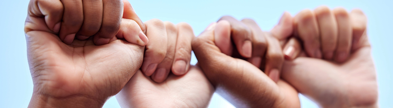Zwei Paar Hände bilden quasi eine Kette. Die eine Faust hält den Daumen einer anderen Hand.