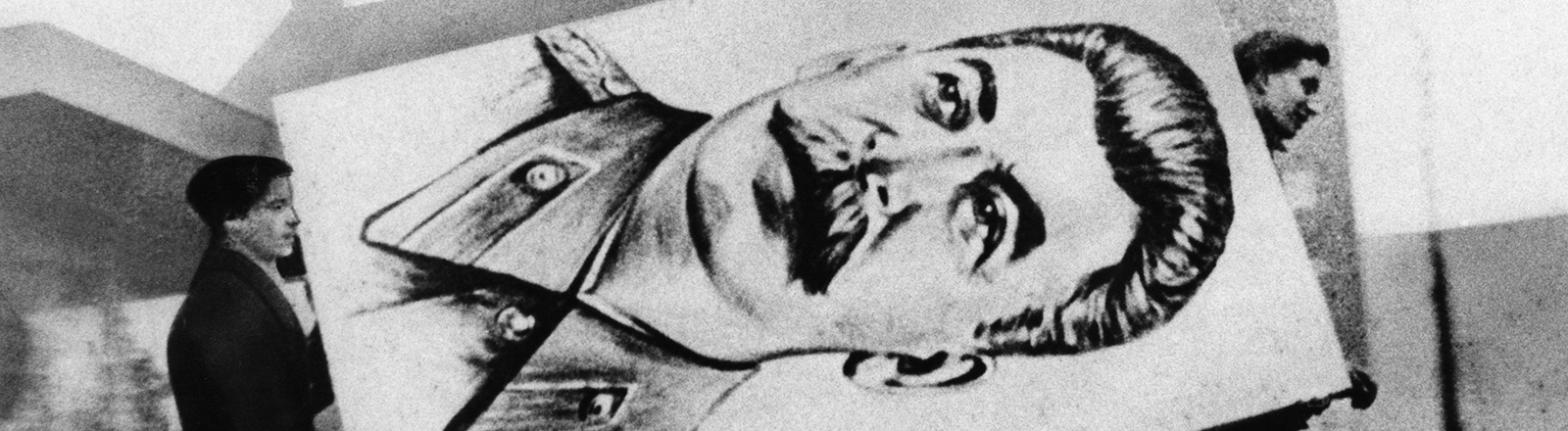 Archivfoto in schwarz-weiß aus dem Jahr 1956: Zwei Männer tragen ein Plakat mit dem Konterfei des Diktators Stalin weg.