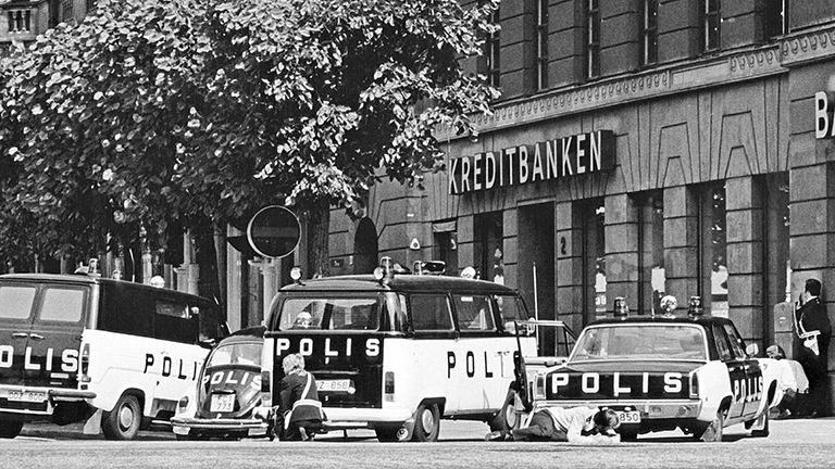 Archivfoto in schwarz-weiß: Polizeiautos stehen vor einem Gebäude. Kreditbanken und Bank steht an dem Haus. Es ist die Geiselnahme in Stockholm im August 1973.