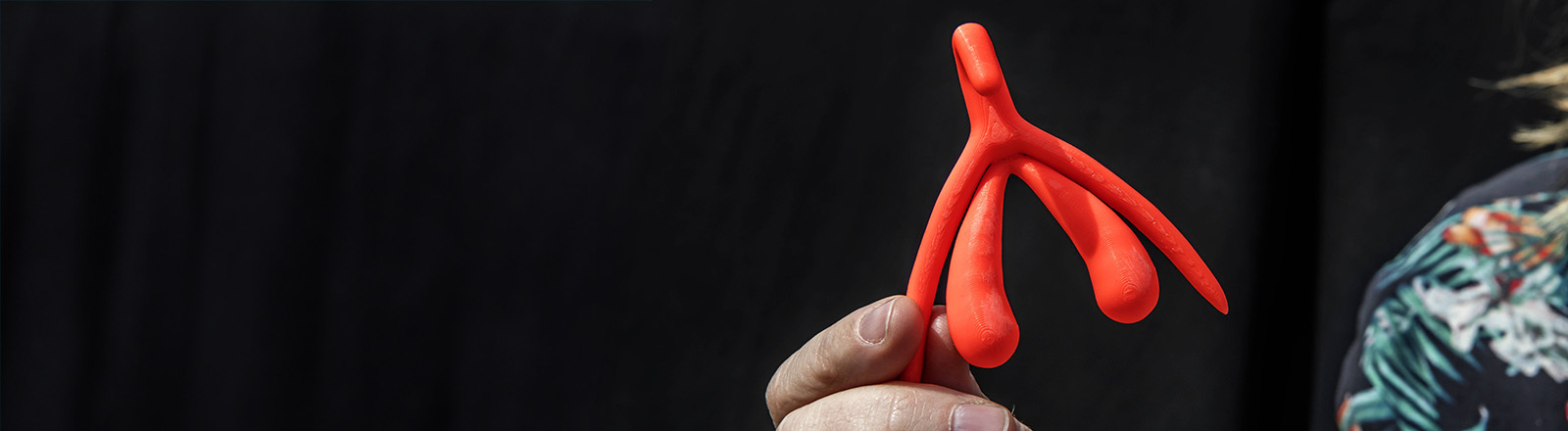 Eine Hand hält einen 3D-Druck einer Klitoris in roter Farbe.
