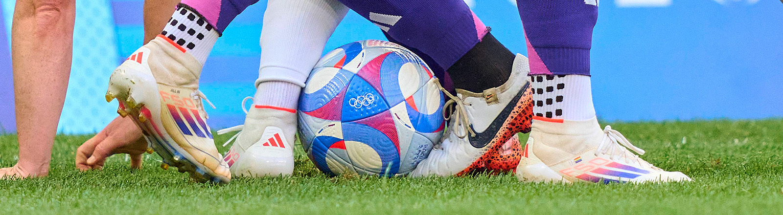 Szene im Frauenfußball bei der olympischen Halbfinalpartie Deutschland gegen die USA 2024. Zu sehen sind die Beine von drei Spielerinnen, die um den Ball kämpfen.