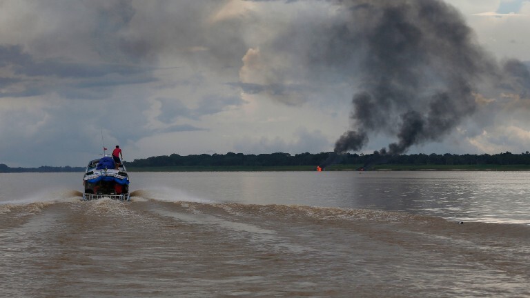 Illegale Goldsucher auf einem Boot auf dem Amazonas. Am Horizont brennender Wald.
