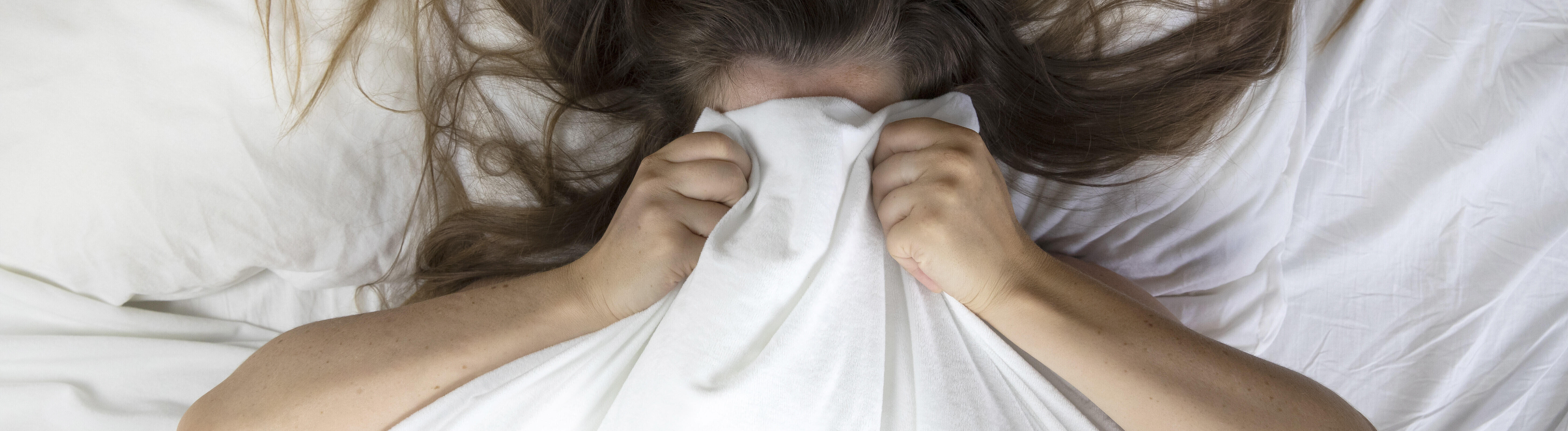 Eine Frau zieht sich im Bett die Decke über im Kopf