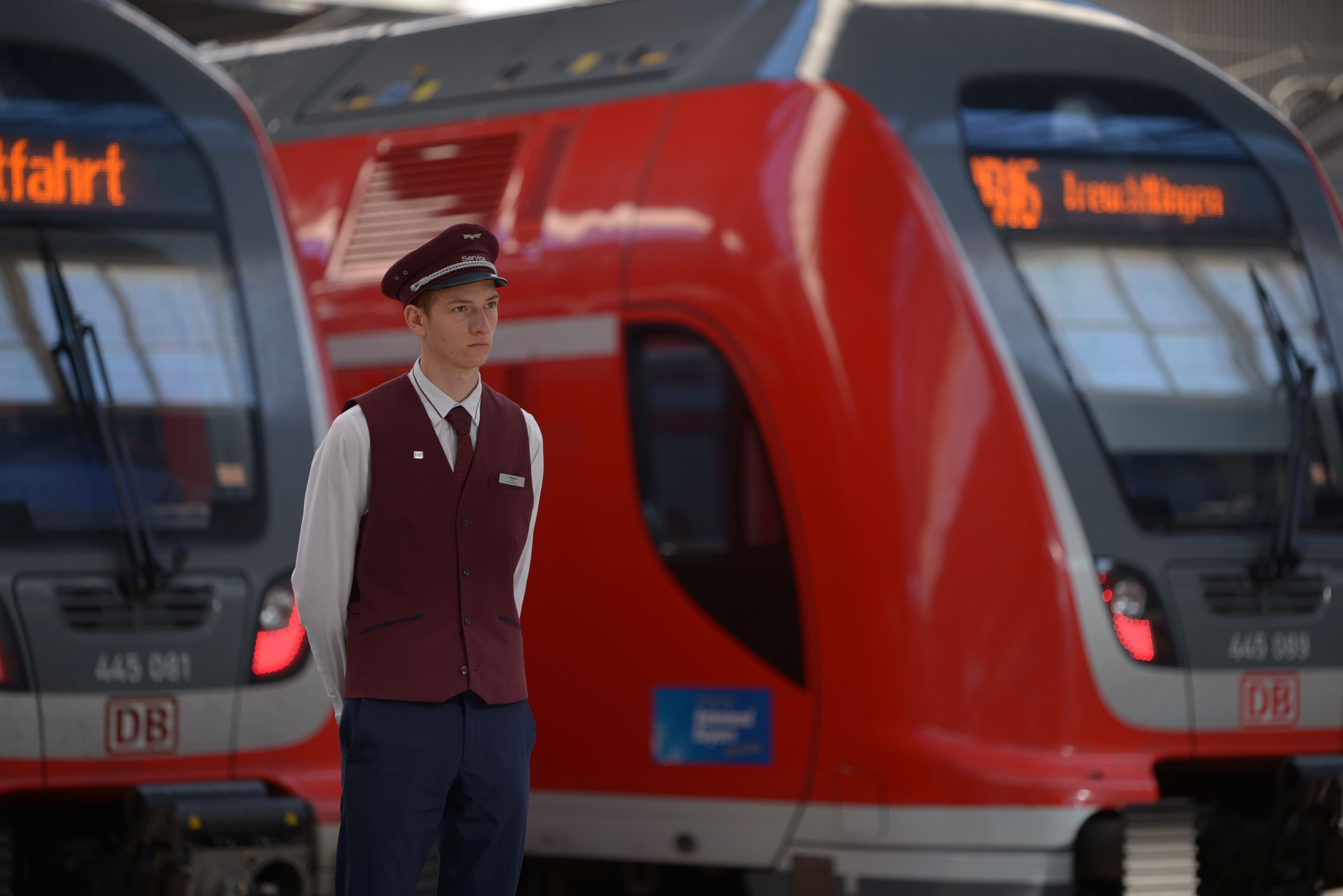 Ein Bahnmitarbeiter steht vor zwei Regionalzügen und schaut in die Ferne.