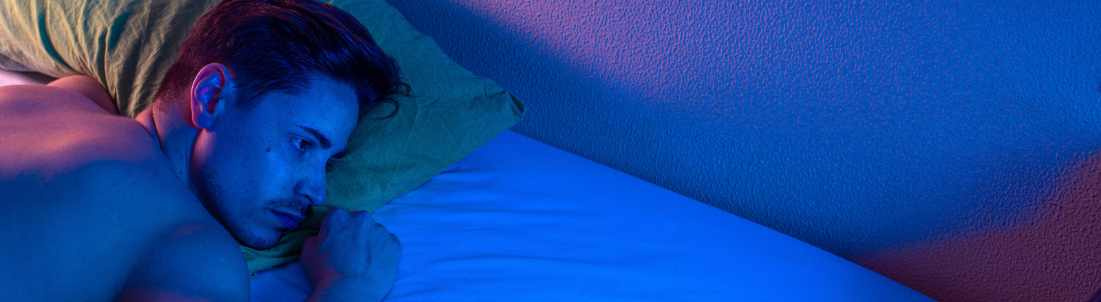 Junger Mann mit Schlaflosigkeit, der nachts versucht einzuschlafen. Nachtlicht ist an.