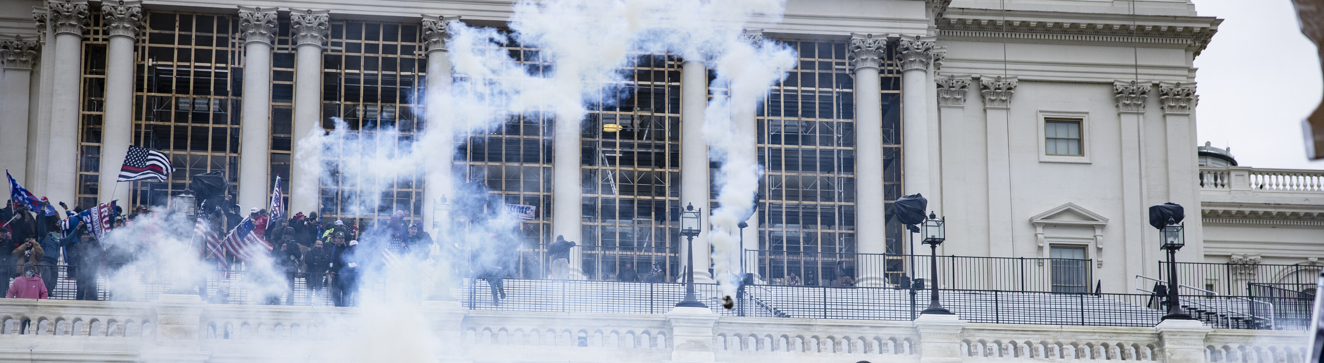 Unterstützer von Donald Trump stürmen das Kapitol in Washington DC, man sieht Flaggen und Rauch