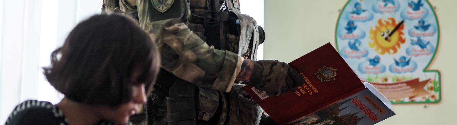 Ein Militär geht mit einem Buch an einem im Klassenraum sitzenden Schulkind vorbei (Kurakhovo, ukrainische und von Russland besetzte Region Donezk, 23.09.2025)