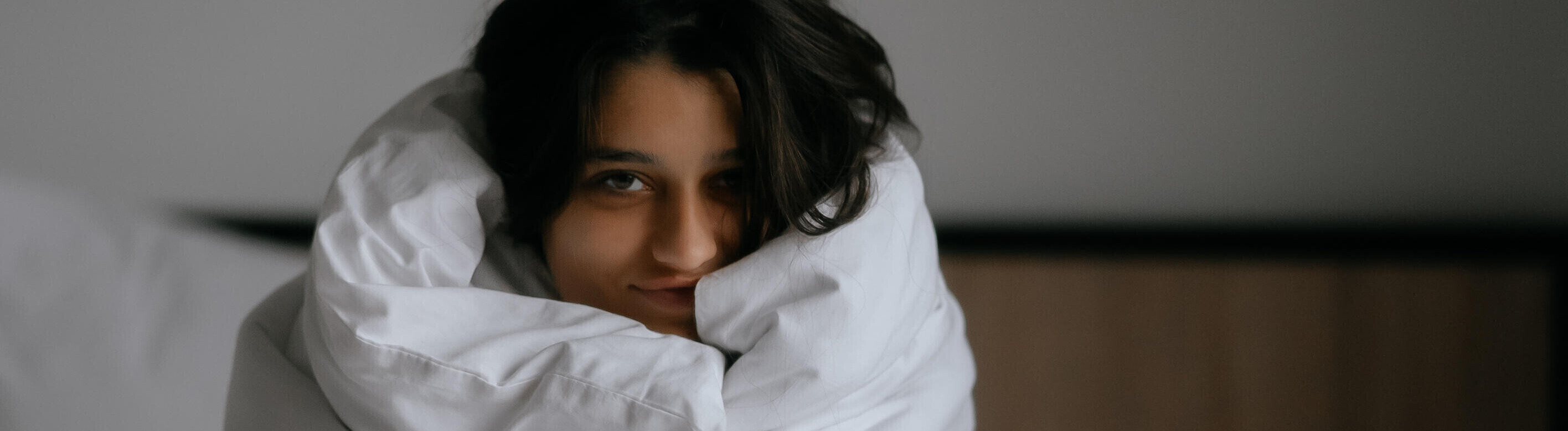 Eine Frau sitzt mit Decke um sich gewickelt im Bett
