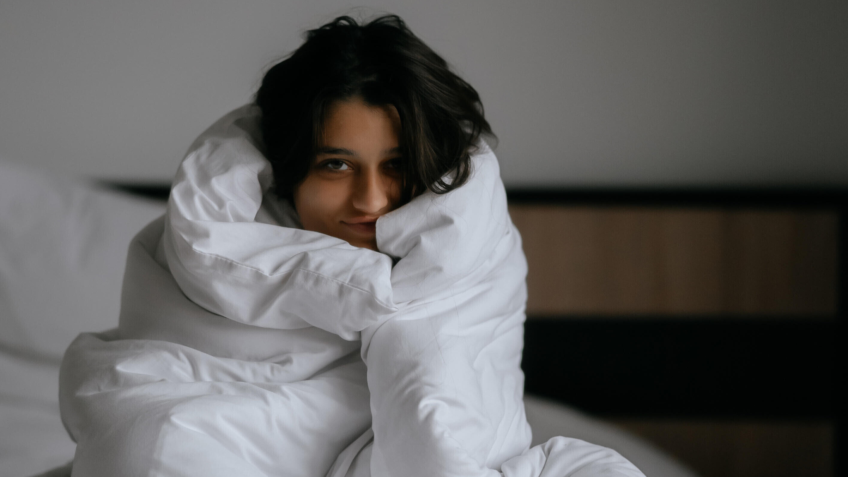 Eine Frau sitzt mit Decke um sich gewickelt im Bett