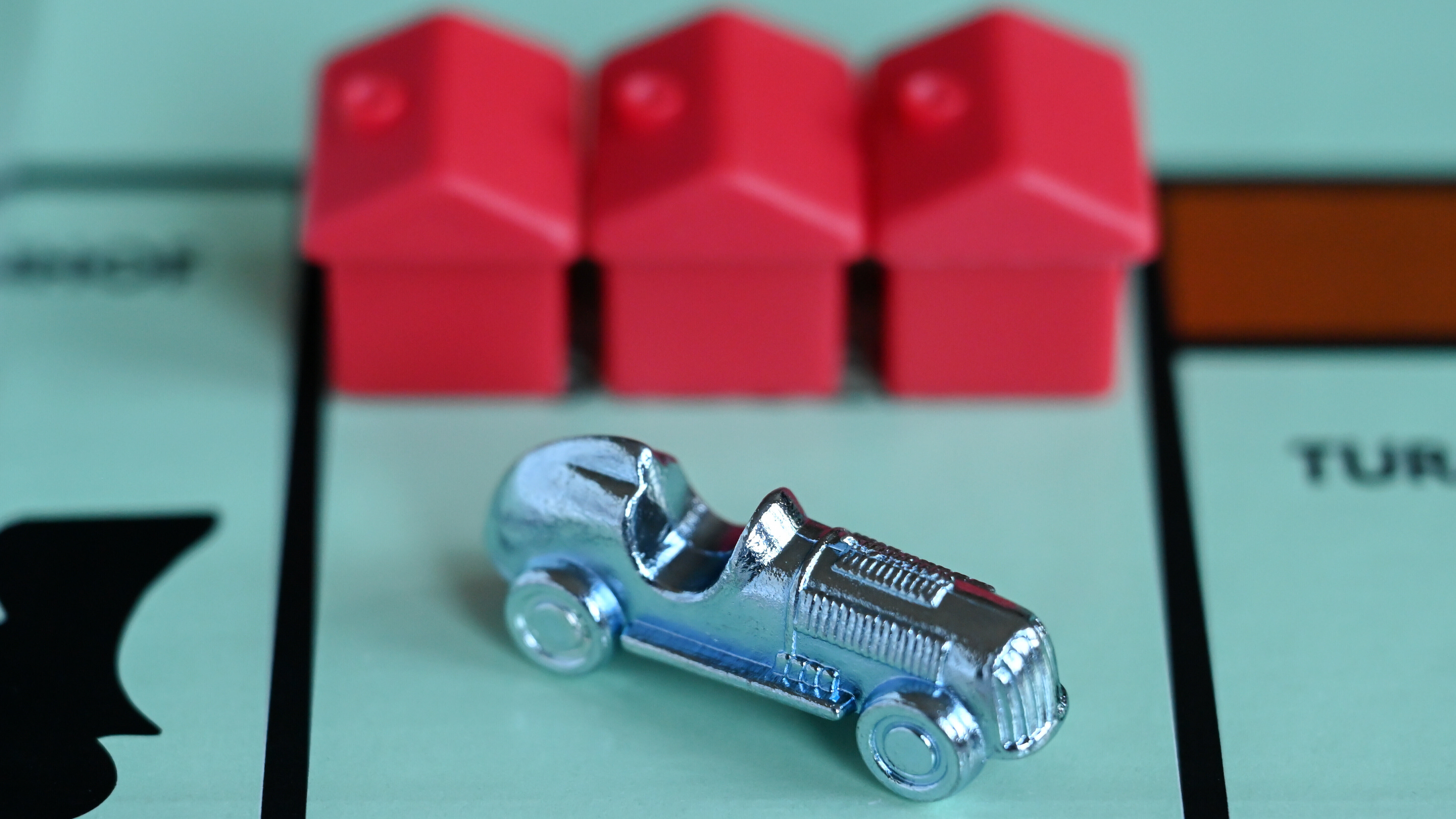 Ein Monopoly-Auto und drei rote Häuschen auf einem Spielfeld