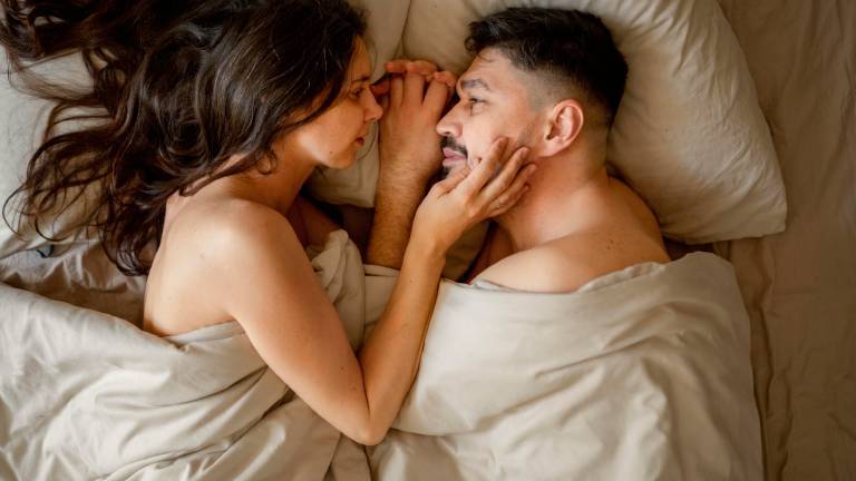 Eine Frau und ein Mann liegen im Bett, schauen sich an und berühren mit den Händen sich zärtlich.