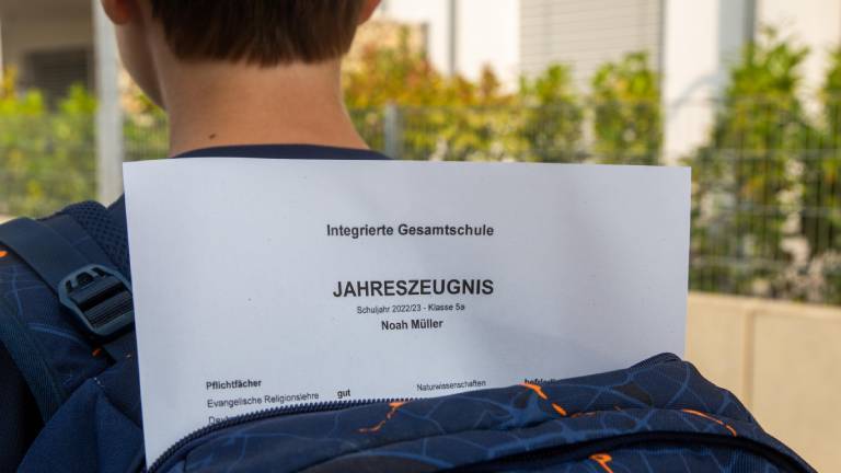 Ein Fünftklässler trägt einen offenen Schulrucksack. Sein Zeugnis ragt aus dem Rucksack heraus.