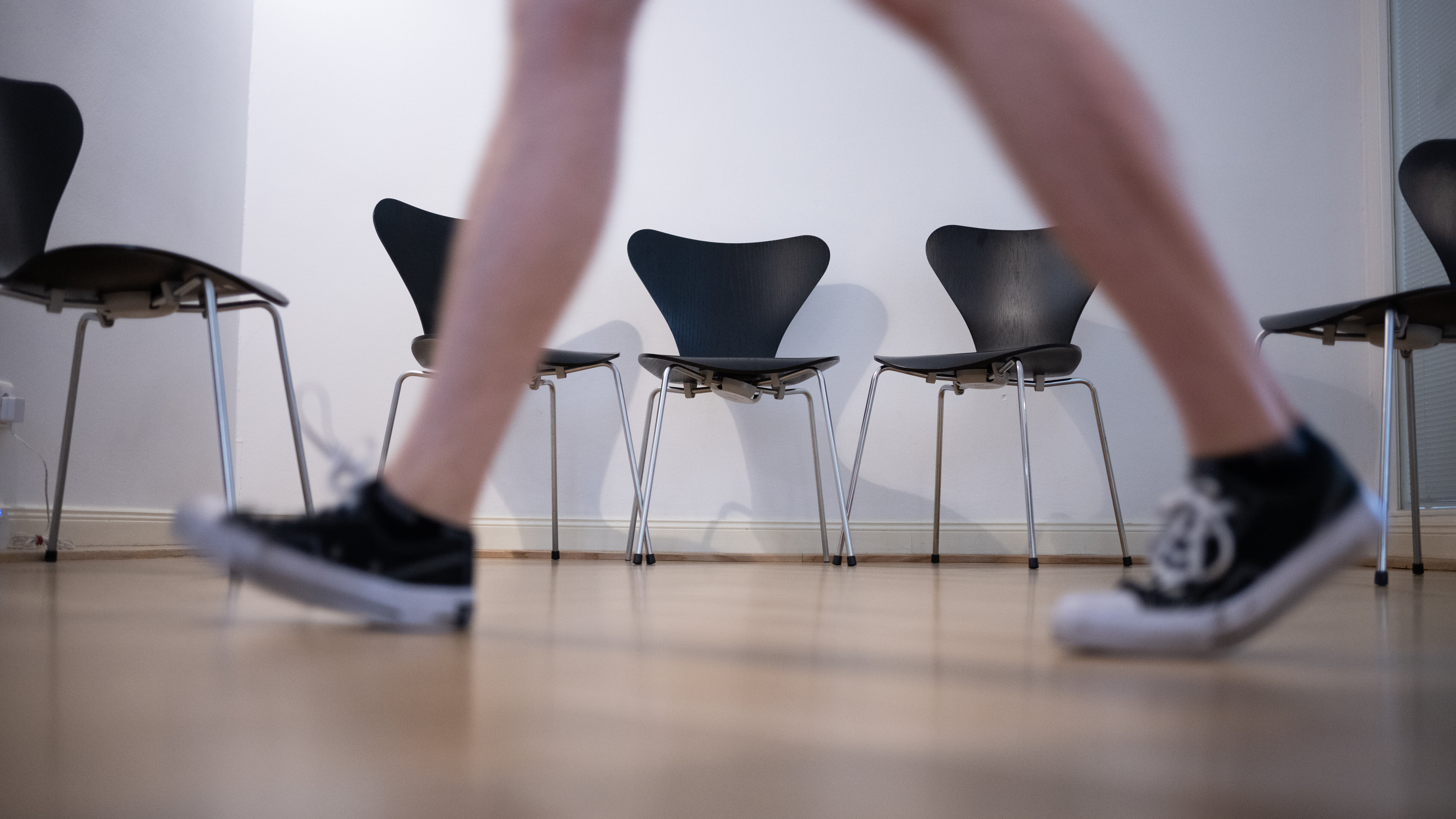 Sneaker tragende Person geht auf einem Gang an einer Reihe von Stühlen vorbei