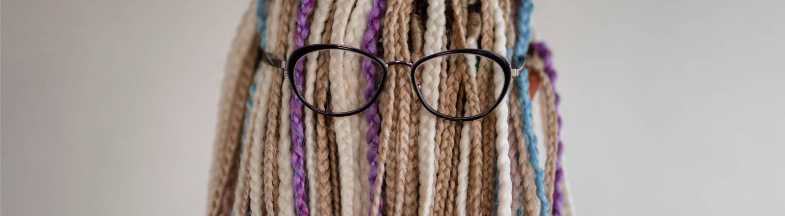 Eine Person mit vielen geflochtenen Zöpfen und einer Brille, das Gesicht ist nicht zu erkennen