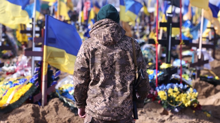 Ein Ukrainischer Soldat steht auf einem Friedhof in Kharkiw vor den Gräbern im Krieg gefallener Ukrainischer Soldaten .
