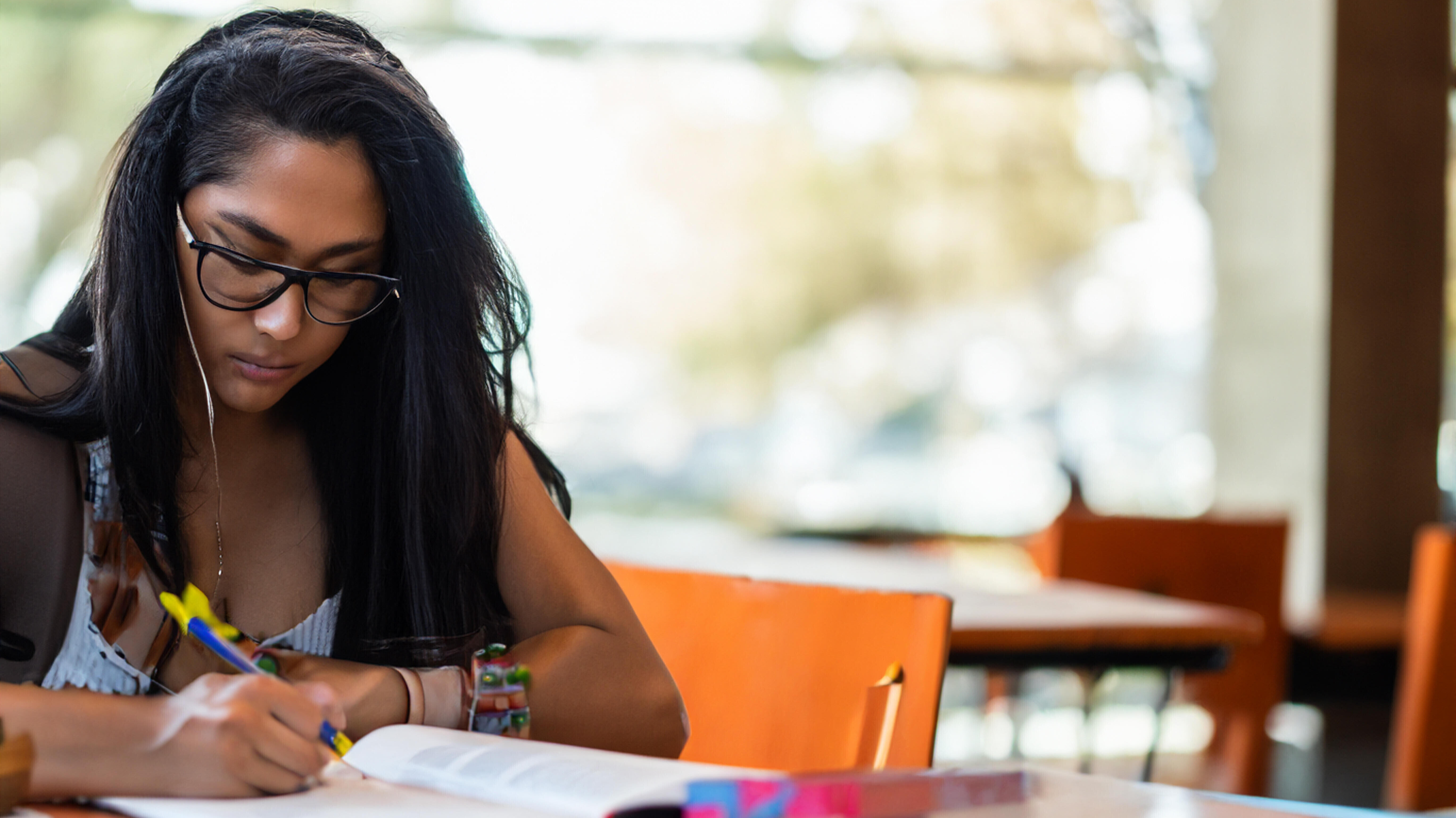 Eine Frau sitzt an einem Tisch und beugt sich über ein Buch, in dem sie Stellen mit einem Stift markiert.