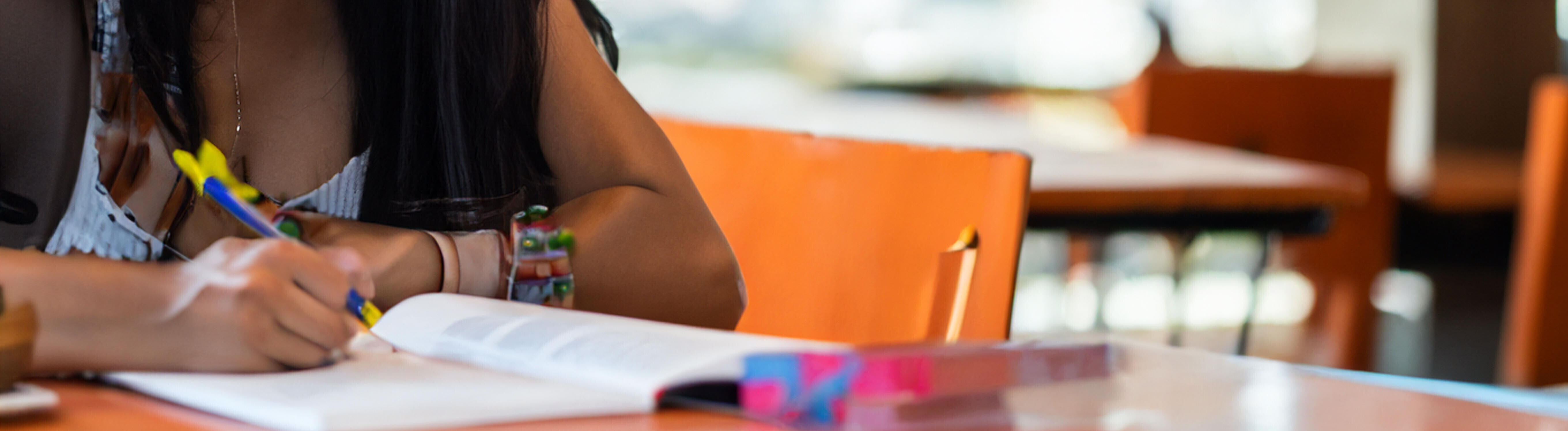 Eine Frau sitzt an einem Tisch und beugt sich über ein Buch, in dem sie Stellen mit einem Stift markiert.