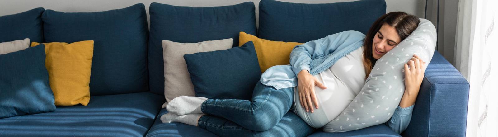 Eine schwangere Frau schläft auf einem Sofa im Wohnzimmer.
