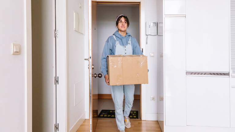 Eine junge Frau trägt einen Umzugskarton in eine Wohnung