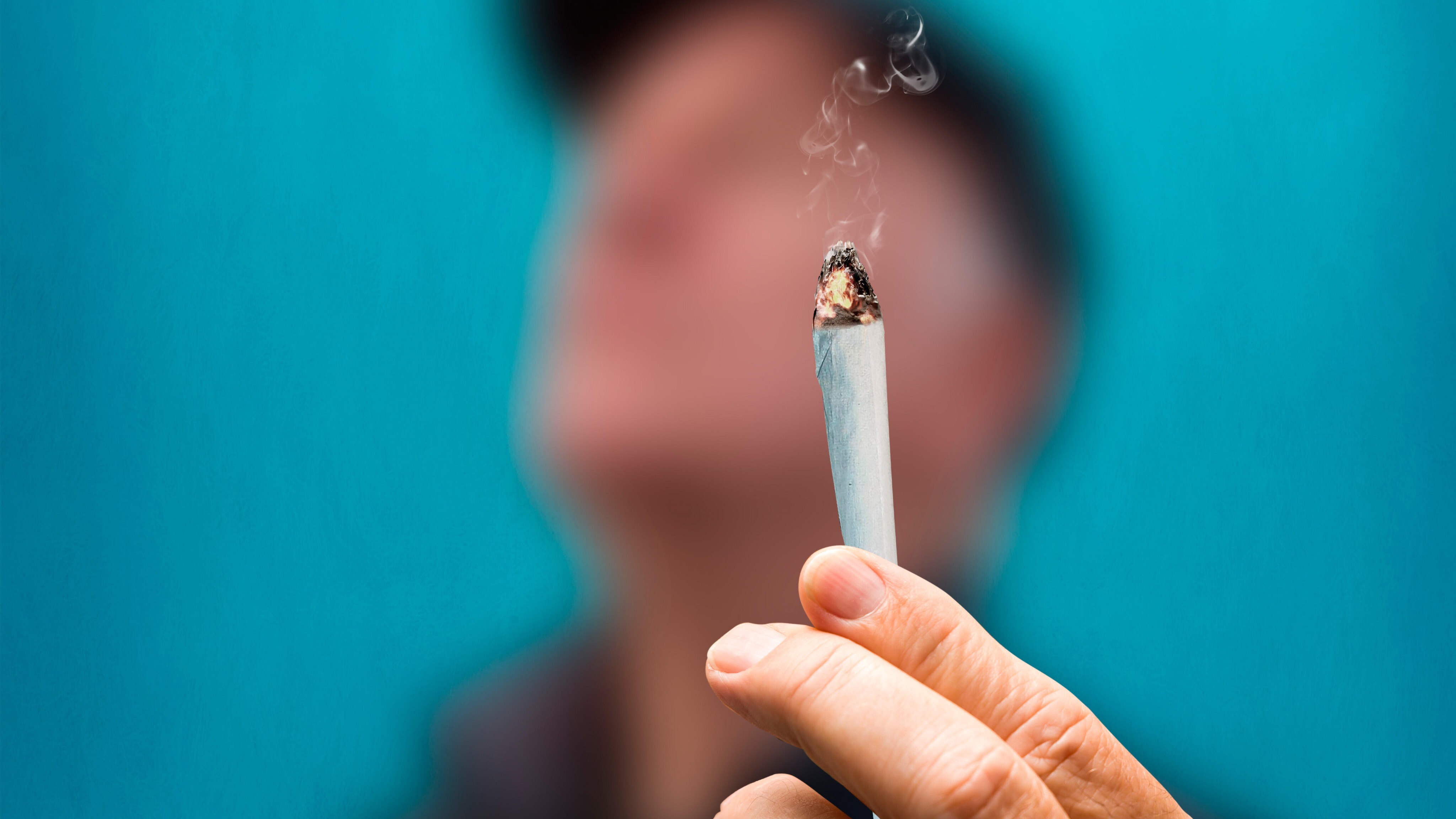 Ein Mann hält einen Joint in die Kamera.