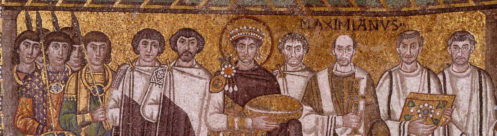 Ein byzantinisches Goldmosaik zeigt Kaiser Justinian den Ersten in purpurnem Gewand im Zentrum einer Gruppe von Männern, bestehend aus Soldaten mit Schild, Geistlichen in weißen Gewändern und Würdenträgern.