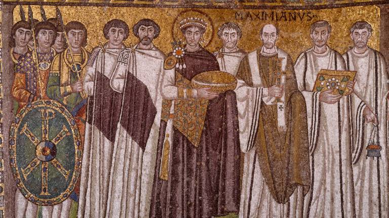 Ein byzantinisches Goldmosaik zeigt Kaiser Justinian den Ersten in purpurnem Gewand im Zentrum einer Gruppe von Männern, bestehend aus Soldaten mit Schild, Geistlichen in weißen Gewändern und Würdenträgern.