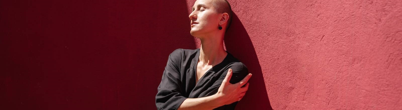 Eine Frau steht vor einer roten Wand und umarmt sich selbst