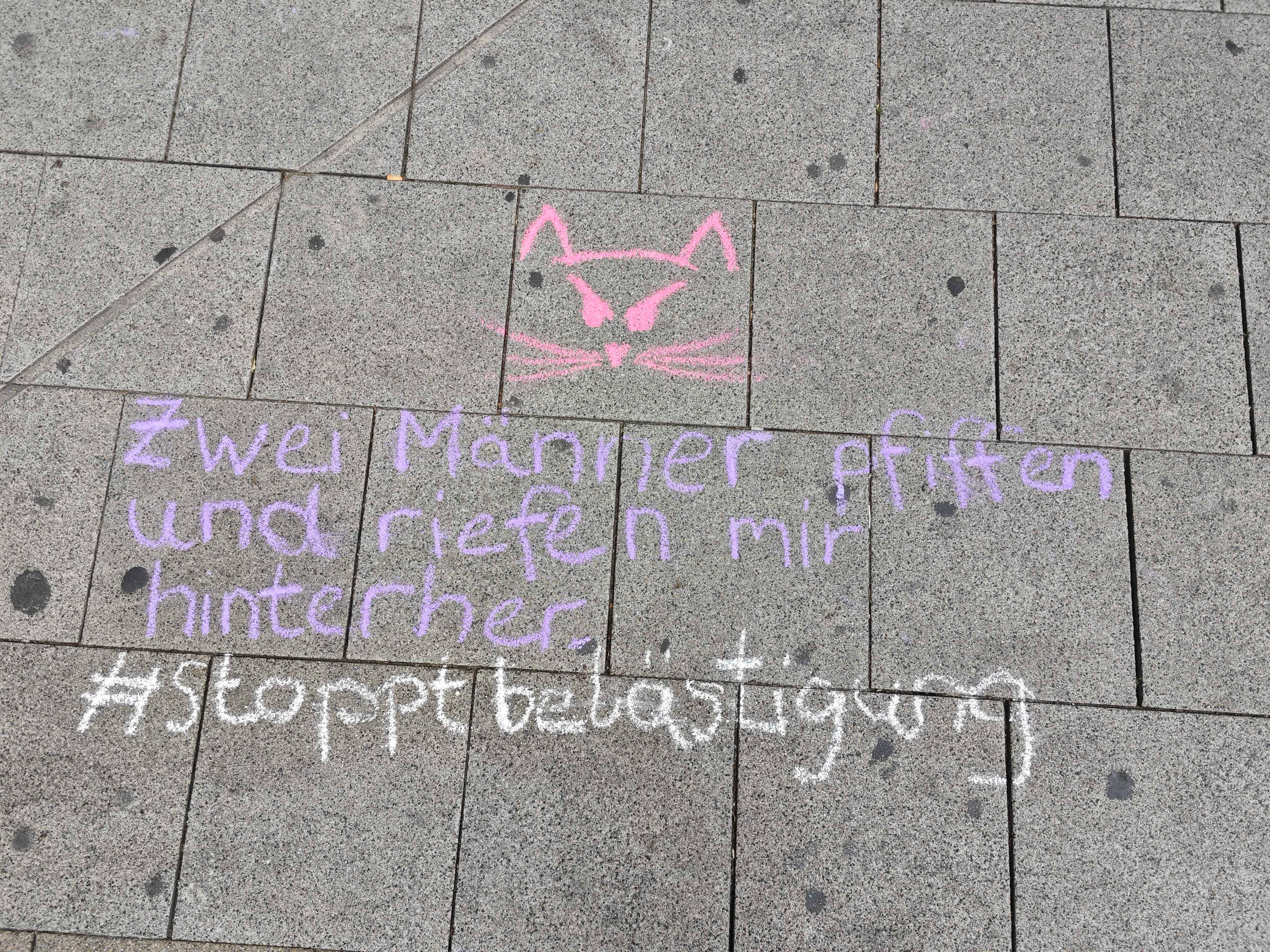 "Zwei Männer pfiffen und riefen mir hinterher - #stoppbelästigung" steht mit Kreide geschrieben auf einer Straße
