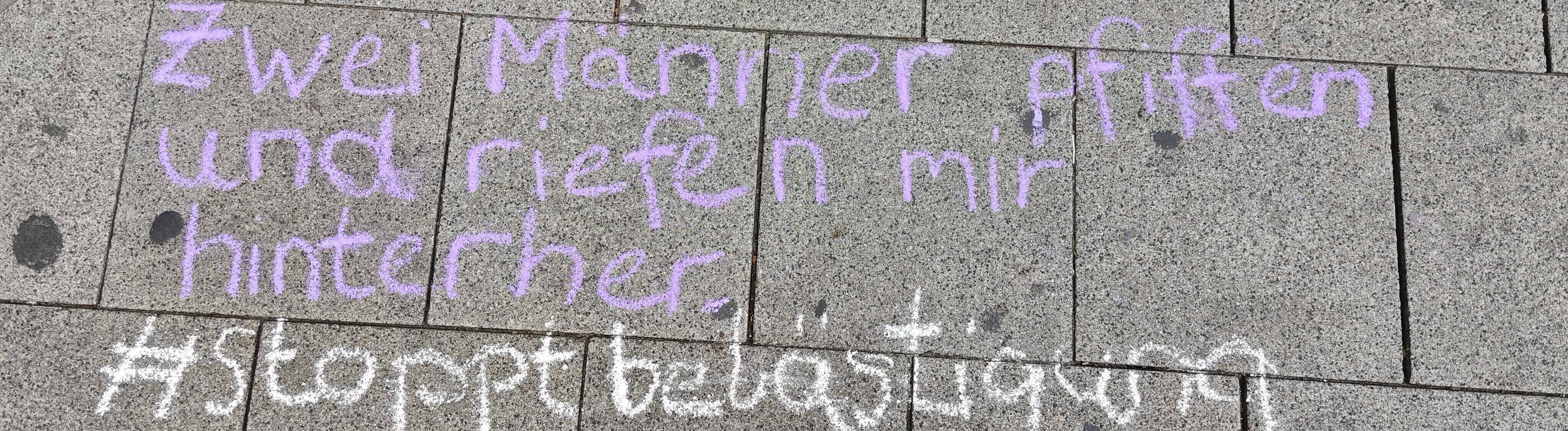 "Zwei Männer pfiffen und riefen mir hinterher - #stoppbelästigung" steht mit Kreide geschrieben auf dem Boden