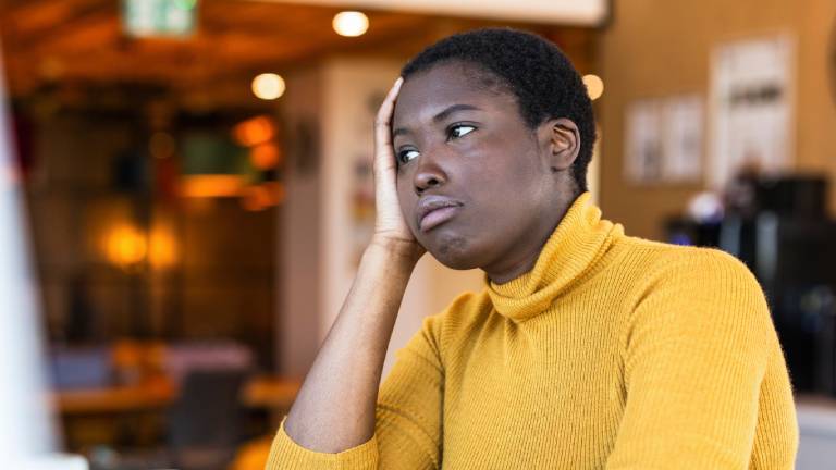 Frau sitzt genervt am Schreibtisch und stützt ihren Kopf auf dem Arm ab