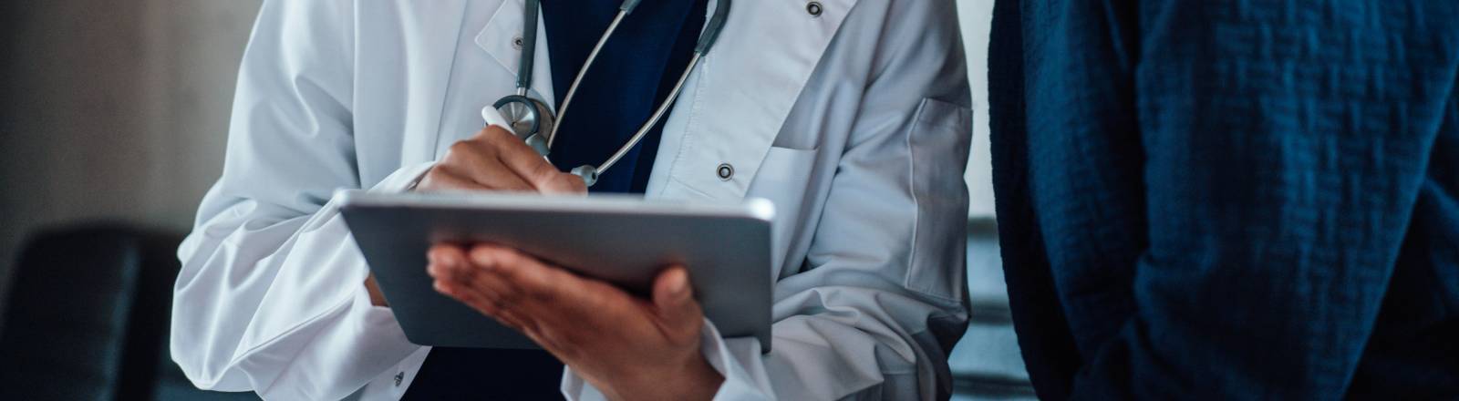 Eine Ärztin mit Stethoskop schaut mit einer Patientin auf ein Tablet.