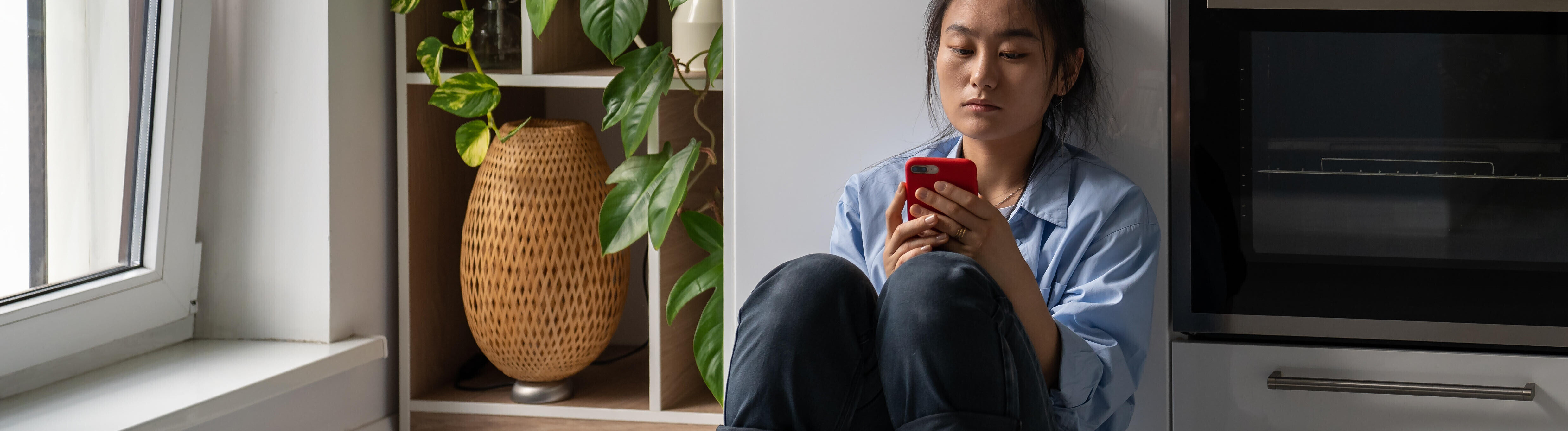 Eine Frau hält ihr Handy in der Hand und blickt mit ernstem Blick auf das Display.